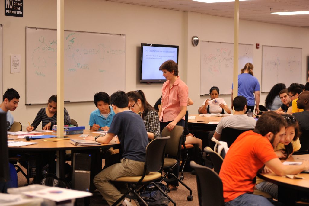 College teacher with student groups at round tables