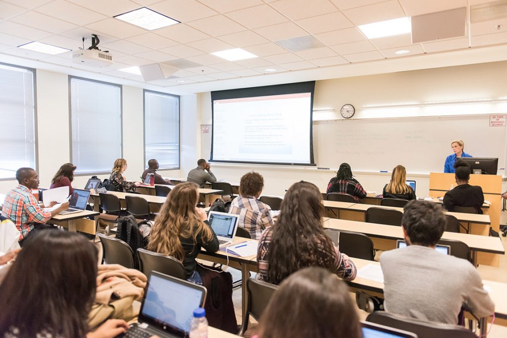 Diverse students with laptops open listening to college professor