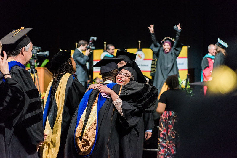 Student and professor embracing at commencement surrounded by celebrations