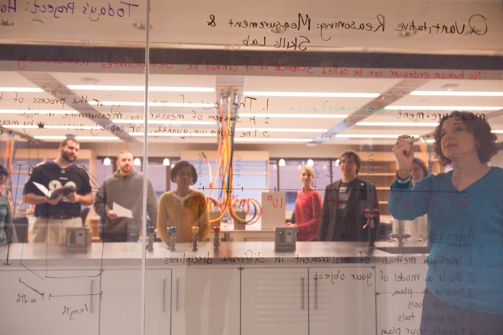 View of teacher writing through glass pane with students looking on