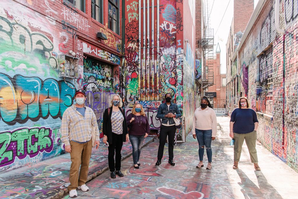 Six touring students in a city alley covered with colorful graffiti