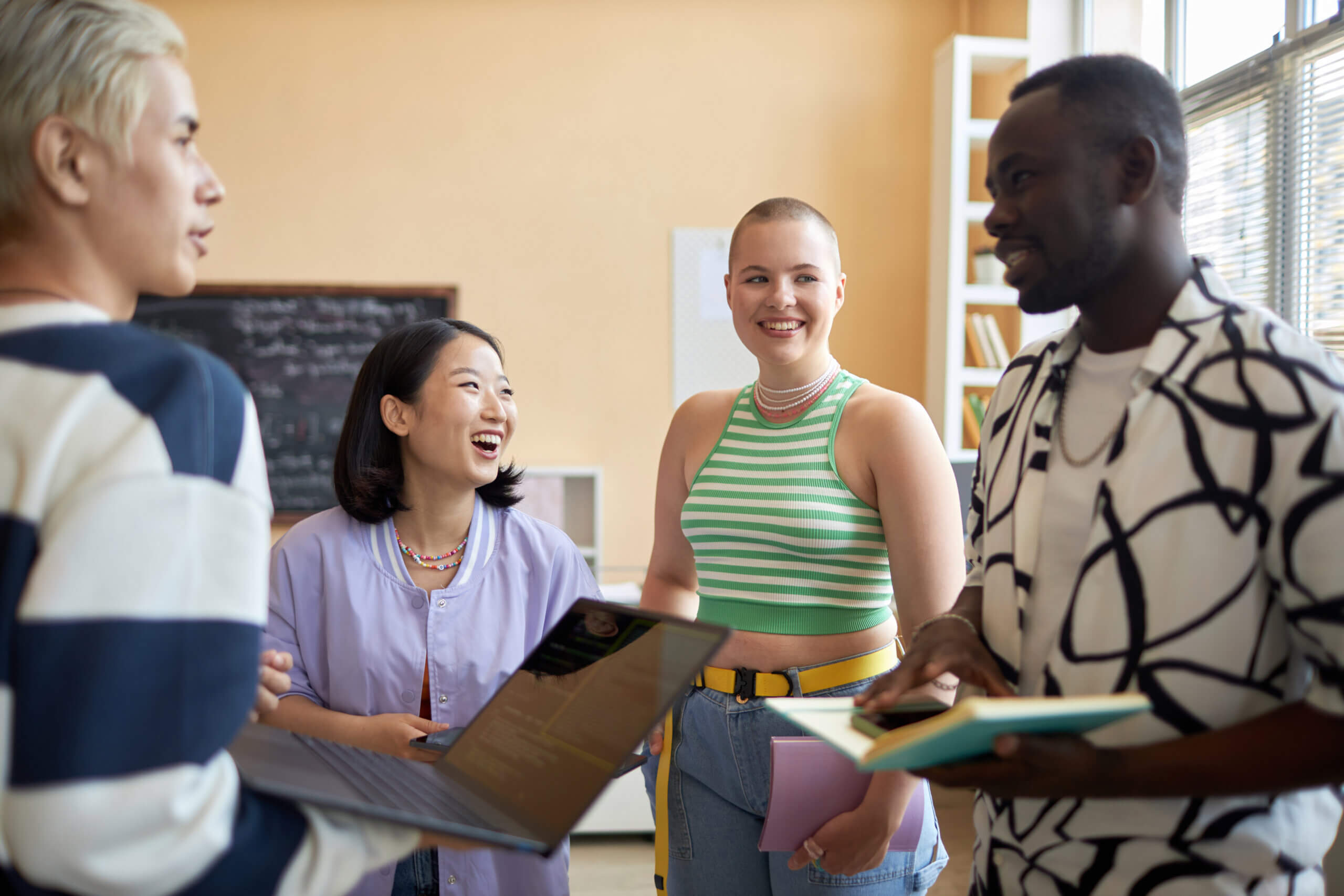 Young laughing Asian woman and her classmate looking at African American guy explaining them his point of view about setting goals for grad school.
