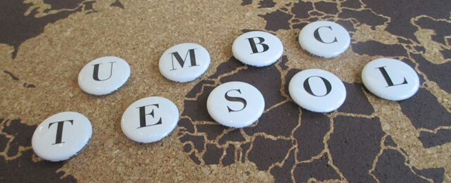 Round, white, tokens sitting on top of a sepia map. Each token has a letter on it writing out UMBC TESOL.