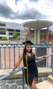 Destiny Hudgins poses with her graduation outfit in front of a waterfall.