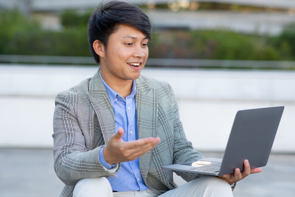 Asian man talking to someone on a laptop, enjoying an informational interview.