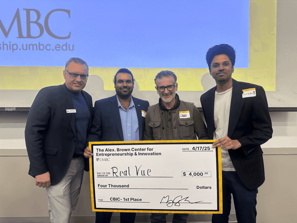 Four men on stage at UMBC holding an oversized $4,000 first-place award check from the Alex. Brown Center for Entrepreneurship and Innovation.