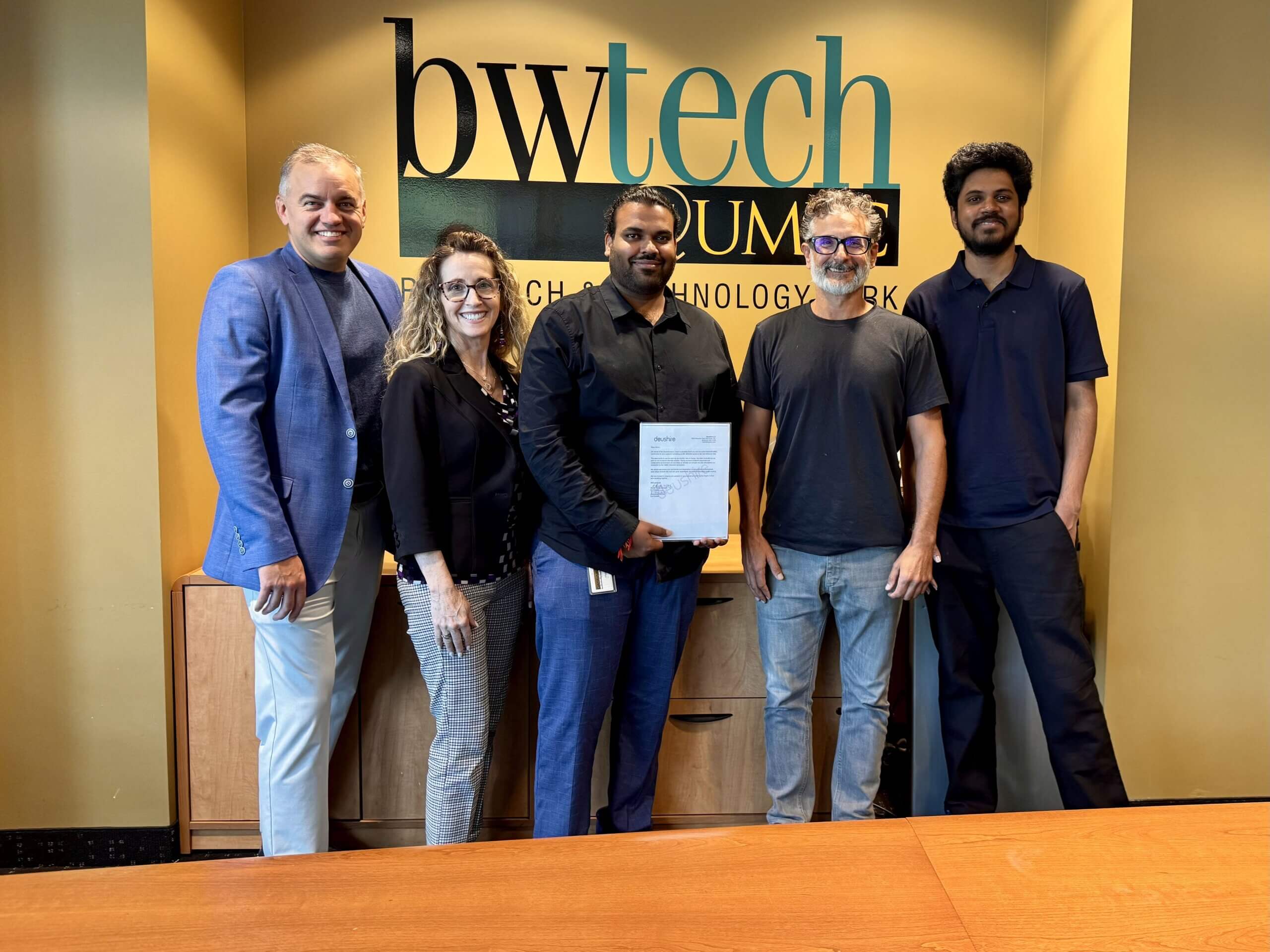 Team members standing together at bwtech@UMBC, holding a signed agreement, celebrating progress on their startup venture.