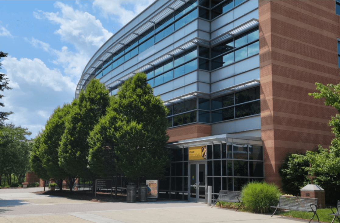 UMBC campus building with glass windows, red brick walls, and trees along the walkway.