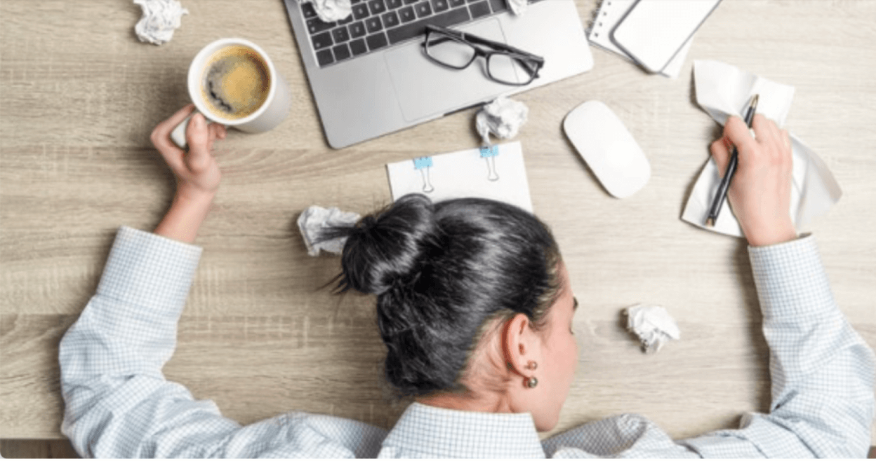 Overwhelmed professional resting head on desk surrounded by coffee, laptop, and crumpled papers — a reminder to prevent burnout through balance and self-care.